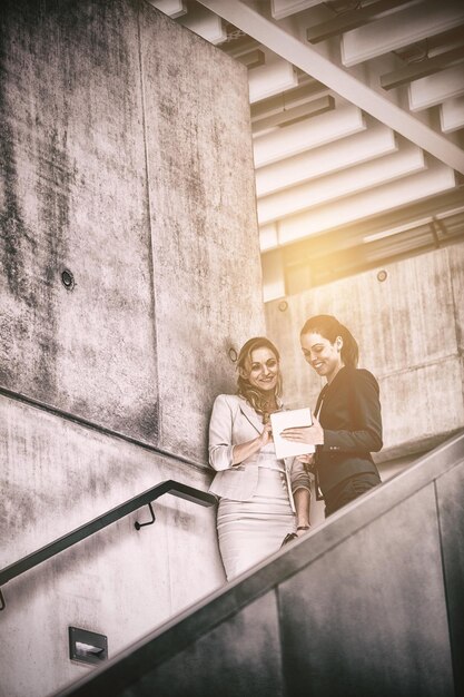 Mujeres empresarias de pie en la escalera y usando tableta