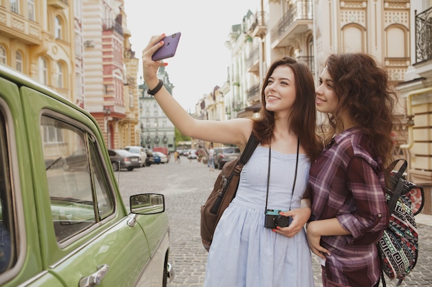 Mujeres encantadoras que se toman selfies mientras hacen turismo en la ciudad, copie el espacio