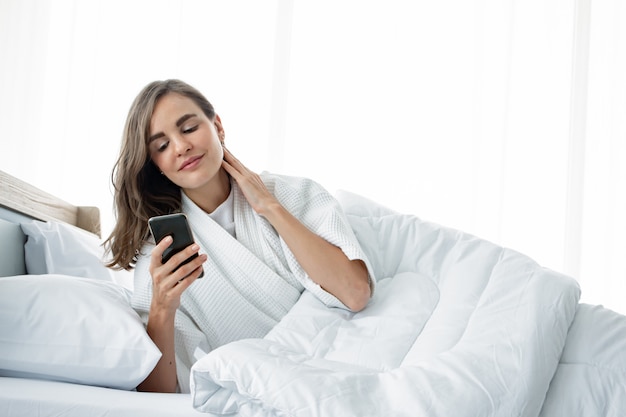 Las mujeres están jugando un teléfono móvil en la cama después de despertarse.