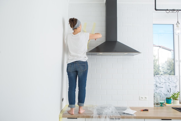 Las mujeres están preparando la pared para pintar Pegando cinta adhesiva a la pared