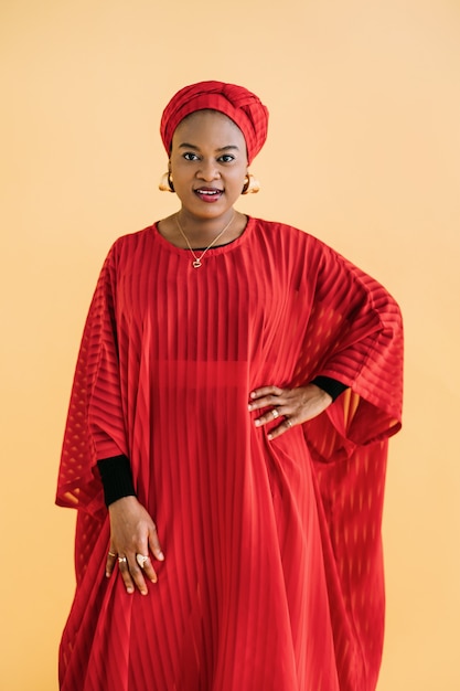 Mujeres en estilo tradicional africano. Tiro de estudio de cintura para arriba de hermosa mujer africana en vestido rojo, pañuelo en la cabeza y joyas posando sobre fondo amarillo y mirando a cámara.