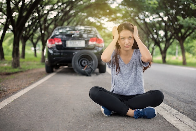 Mujeres estresadas sentadas después de una avería del coche con el triángulo rojo de un automóvil en el camino
