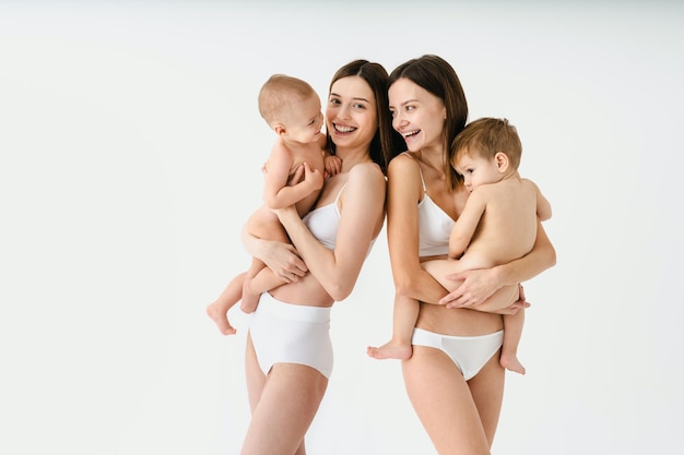 Mujeres felices sosteniendo a sus bebés con antecedentes coloreados - Mujeres jóvenes usando ropa interior cuidando a sus hijos pequeños - Concepto de embarazo, maternidad, personas y expectativas