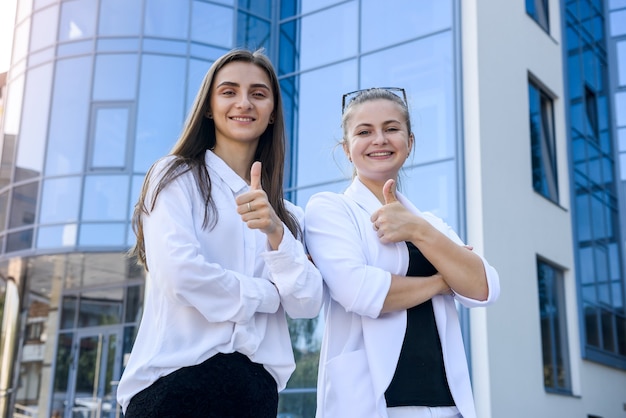 Mujeres felices en trajes de negocios con carpeta de pie antes de la oficina de grandes empresas