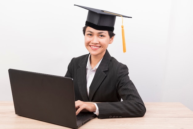 Mujeres graduadas con un sombrero negro sentado en un escritorio sonriendo.