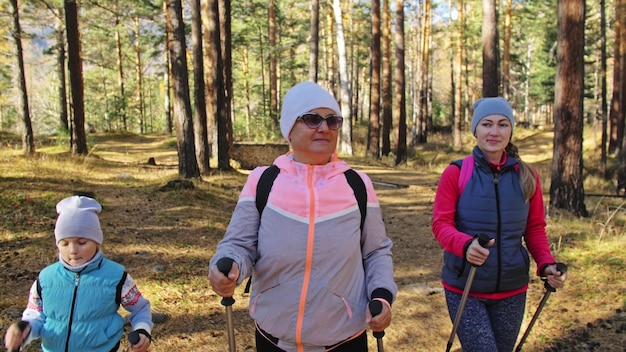 Las mujeres hacen marcha nórdica en la naturaleza, las niñas y los niños usan bastones de trekking y mochilas de bastones nórdicos.