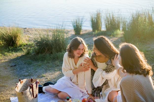 Foto mujeres hermosas jóvenes de 25 años en un picnic de otoño cerca del lago vaso de pasteles de vino blanco