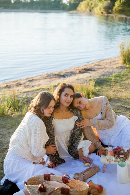 Foto mujeres hermosas jóvenes de 25 años en un picnic de otoño cerca del lago vaso de pasteles de vino blanco