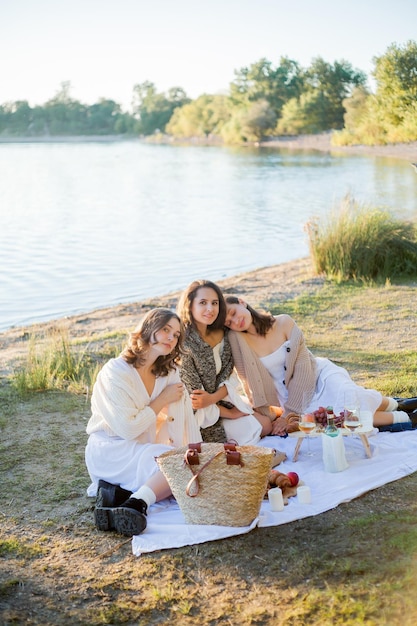 Foto mujeres hermosas jóvenes de 25 años en un picnic de otoño cerca del lago vaso de pasteles de vino blanco