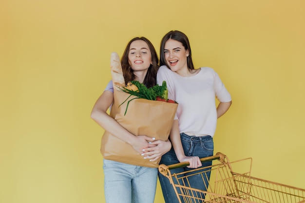 Mujeres hermosas jóvenes sosteniendo una bolsa de papel para llevar de la entrega sobre fondo amarillo