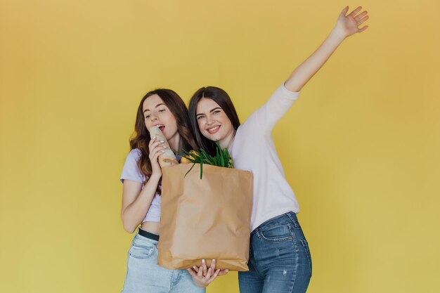 Mujeres hermosas jóvenes sosteniendo una bolsa de papel para llevar de la entrega sobre fondo amarillo