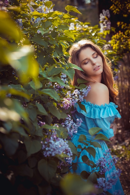 Mujeres hermosas que disfrutan del jardín de la lila, mujeres jovenes con las flores en parque verde. Alegres adolescentes caminando al aire libre. color de estilo de luz suave