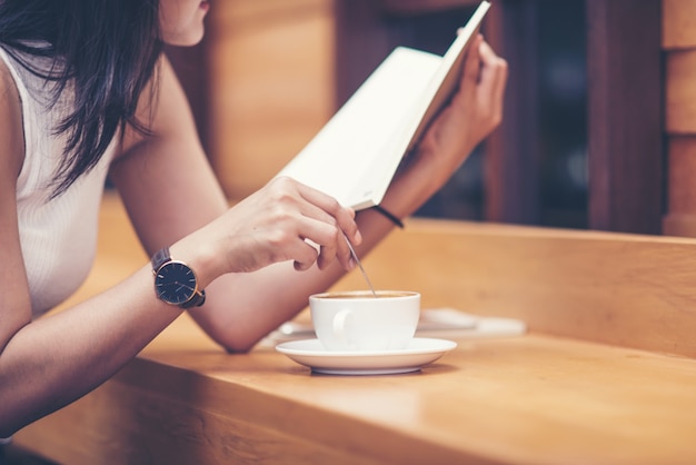 Mujeres hermosas que se sientan por la tabla de madera y el libro de lectura