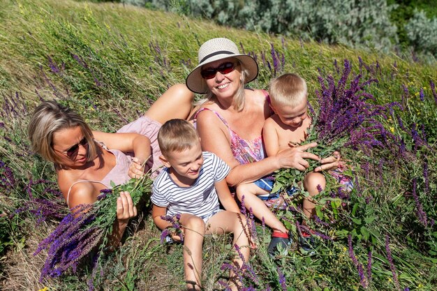 Mujeres con hijos recogen salvia en el campo una mujer joven una abuela en un vestido de lila y sombrero y nietos en pantalones cortos en un soleado día de verano