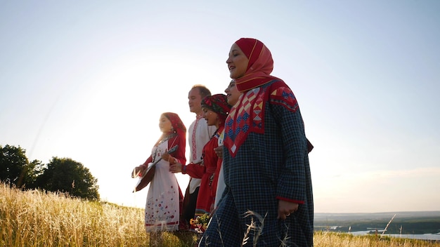 Mujeres y hombres con ropa tradicional rusa caminando en fila en el campo y cantando una canción