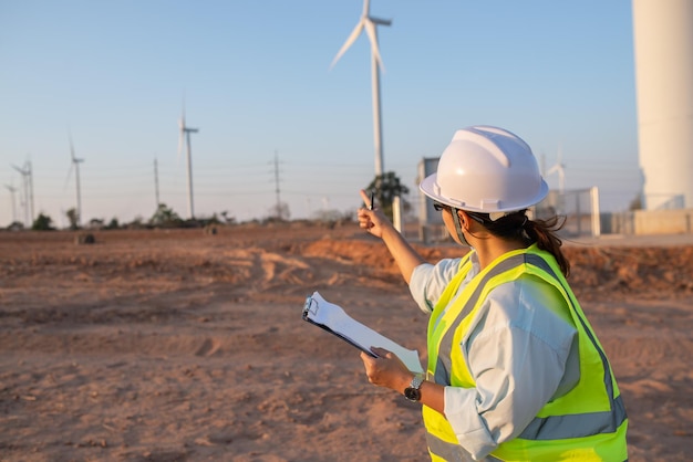 Mujeres ingenieras trabajando y sosteniendo el informe en la estación generadora de energía de la granja de turbinas eólicas en la gente de mountainThailand