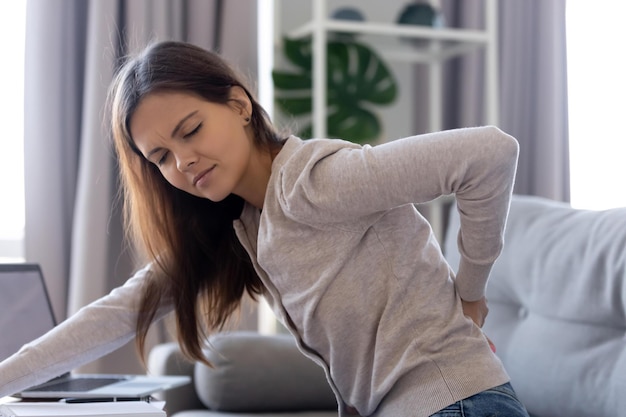 Las mujeres jóvenes agotadas tienen espasmos musculares repentinos en la parte inferior de la espalda después de sentarse en una postura incorrecta. Las mujeres tocan la columna vertebral.