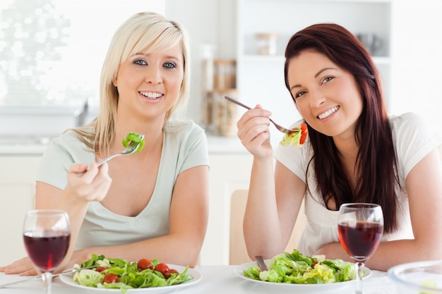 Mujeres jóvenes alegres comiendo ensalada