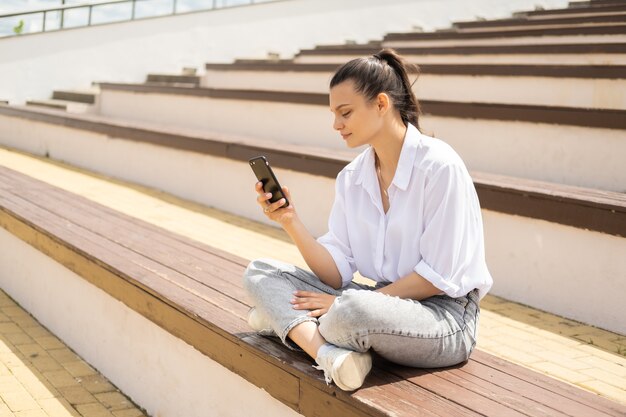 Mujeres jóvenes alegres felices con smartphone disfrutando de día soleado sentado en el anfiteatro.