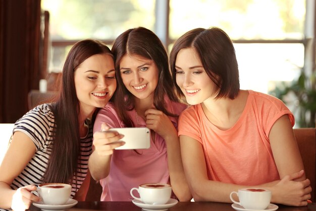 Foto mujeres jóvenes alegres tomando selfie mientras beben café en la cafetería