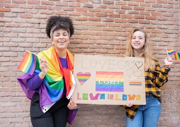 Mujeres jóvenes en la calle disfrutando sosteniendo la bandera del orgullo gay durante la protesta.