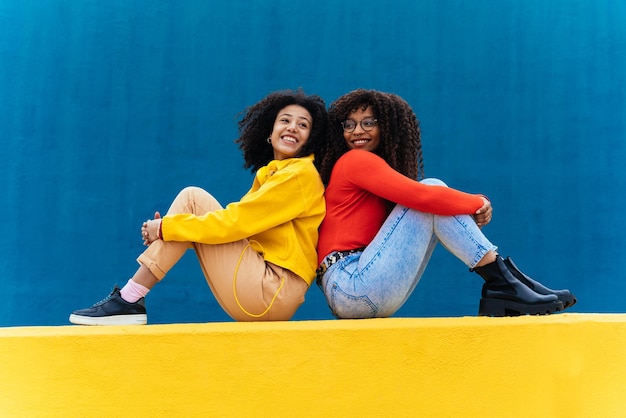 Mujeres jóvenes felices posando en paredes de color azul y amarillo