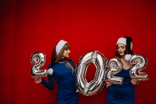 Mujeres jóvenes felices sosteniendo globos plateados 2022 para celebrar Feliz Navidad y Próspero Año Nuevo