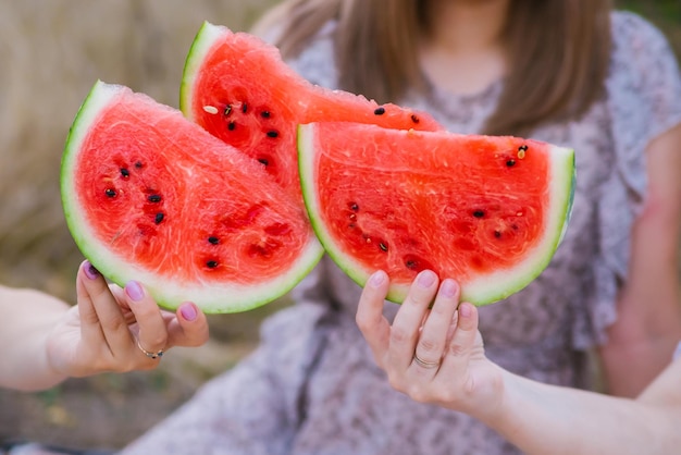 Mujeres jóvenes felices sostienen rodajas de sandía al aire libre Primer plano de rodajas de sandía Baya roja brillante Merienda dulce jugosa en verano en un picnic