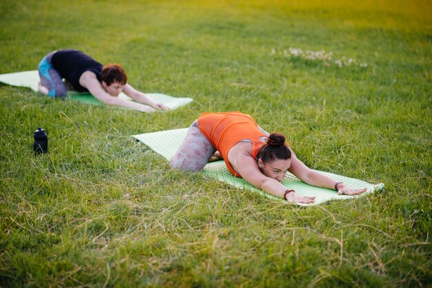 Las mujeres jóvenes hacen yoga al aire libre en el parque durante el atardecer. Estilo de vida saludable