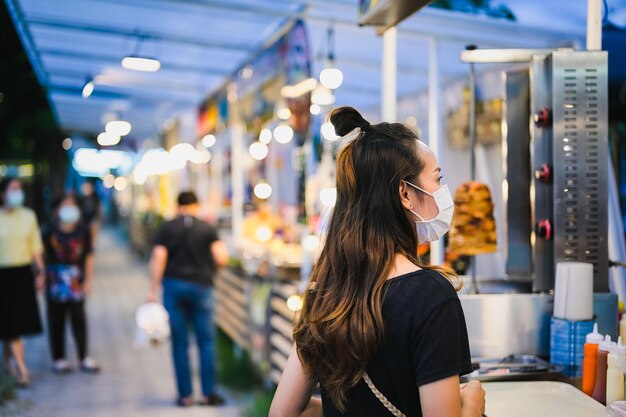 Mujeres jóvenes con máscaras quirúrgicas eligiendo comida en el mercado nocturno de Chiang Mai, al norte de Tailandia
