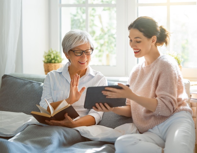 Las mujeres jóvenes y mayores están usando tablet pc. La hija está ayudando a la madre a divertirse en casa.