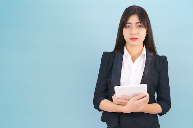 Las mujeres jóvenes de pie en traje sosteniendo su tableta digital computor contra el fondo azul.