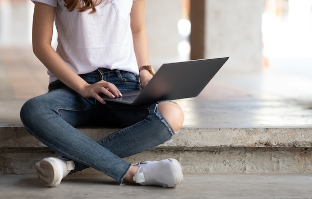 Mujeres jovenes que usan la computadora portátil en la pierna.