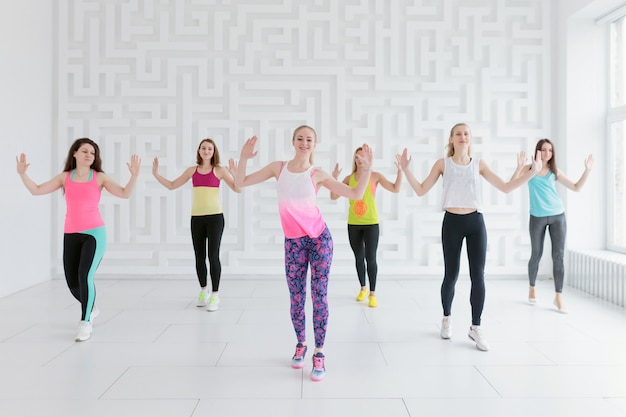 Mujeres jóvenes en ropa deportiva colorida en la clase de fitness de baile en el gimnasio blanco