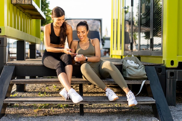 Mujeres jóvenes en ropa deportiva mirando el teléfono móvil después del entrenamiento físico