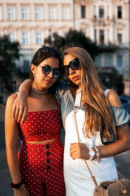 Mujeres jóvenes serias en traje de verano y gafas de sol pasando un buen rato juntos