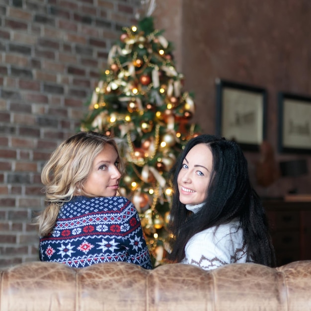 Mujeres jóvenes sonriendo mientras está sentado cerca del árbol de navidad