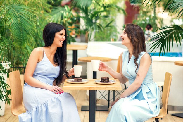 Mujeres jovenes sonrientes con las tazas de café y la paz de la torta en el café.