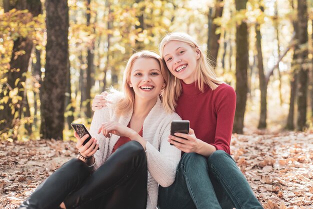 Mujeres jóvenes sonrientes con teléfono celular en otoño parque amistad niñas concepto sonriendo amigas w ...