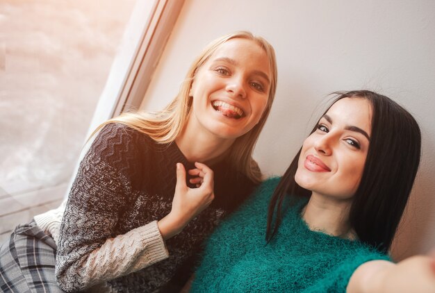 Mujeres jóvenes sonrientes tomando selfie mientras bebe café en el interior en la reunión