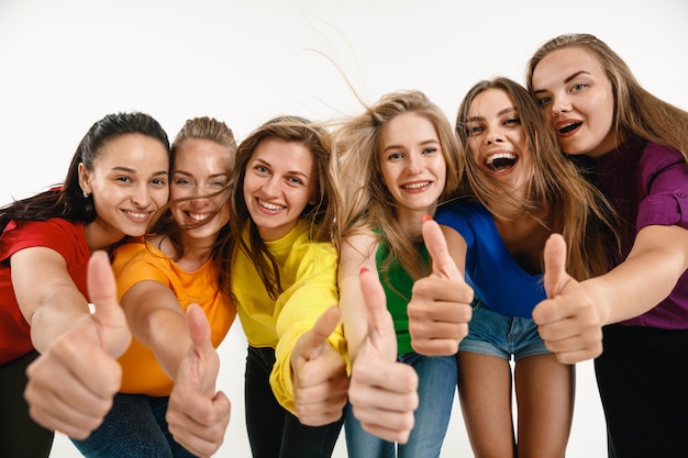 Las mujeres jóvenes vestían los colores de la bandera LGBT aislados en la pared blanca. Modelos femeninos caucásicos en camisas brillantes.