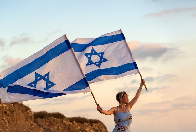 Las mujeres judías patriotas en un vestido azul sostiene la bandera de Israel en sus manos al atardecer al aire libre