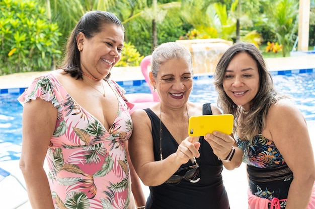 Mujeres latinas tomando selfie junto a la piscina