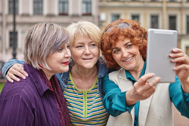 Las mujeres maduras están tomando fotos con una tableta en el exterior.