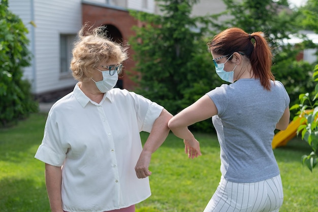 Mujeres con máscaras médicas saludan sus codos afuera Una anciana y su hija adulta mantienen una distancia social en el parque durante la epidemia de coronavirus Nuevo apretón de manos golpeando los codos