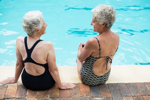 Mujeres mayores interactuando entre sí mientras se relajan junto a la piscina