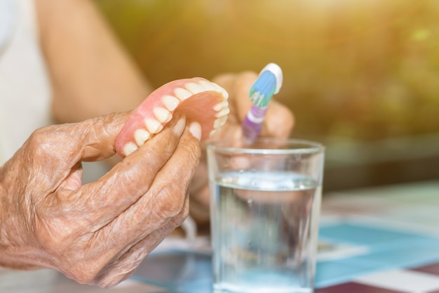 Las mujeres mayores sostienen los dientes falsos con sucio para la limpieza de la prótesis parcial removible con un cepillo de dientes