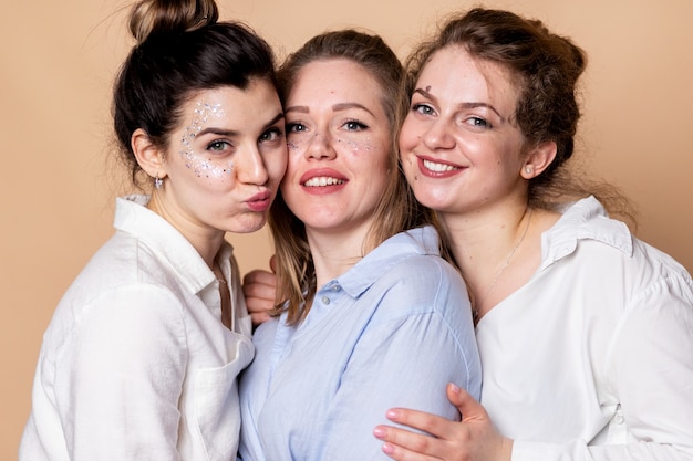 Mujeres multiculturales felices y con sobrepeso en sujetadores aislados en beige. Belleza diversa. Tres señoras multiétnicas envueltas en toallas de baño posando sonriendo en la pared beige.