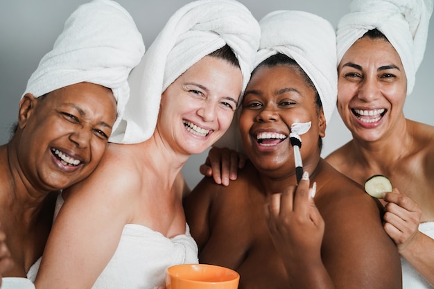 Foto mujeres multigeneracionales que se divierten aplicando máscaras faciales de belleza en la cara: enfoque principal en la cara de la mujer caucásica