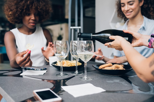 Mujeres multirraciales jóvenes sentadas en un restaurante moderno y bebiendo juntas